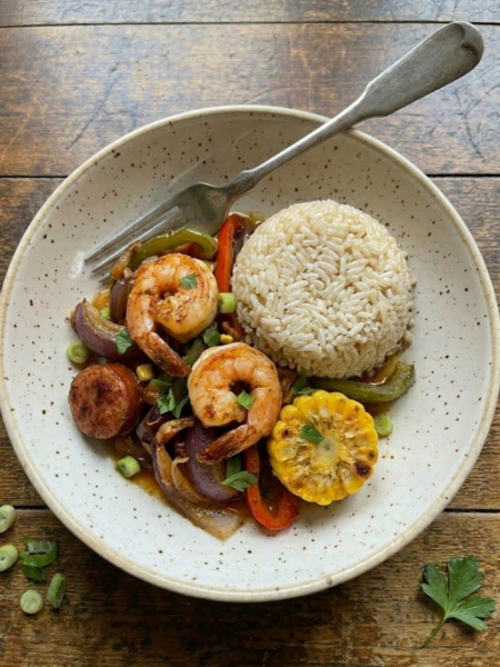 Cajun shrimp, smoked sausage, roasted corn, peppers, and rice served in a bowl with buttery Cajun sauce.