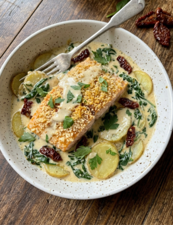 Creamy Tuscan salmon with potatoes, spinach, and sun-dried tomatoes in parmesan sauce.
