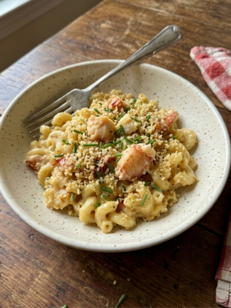 Creamy lobster mac and cheese with crispy panko and chives served in a ceramic bowl.