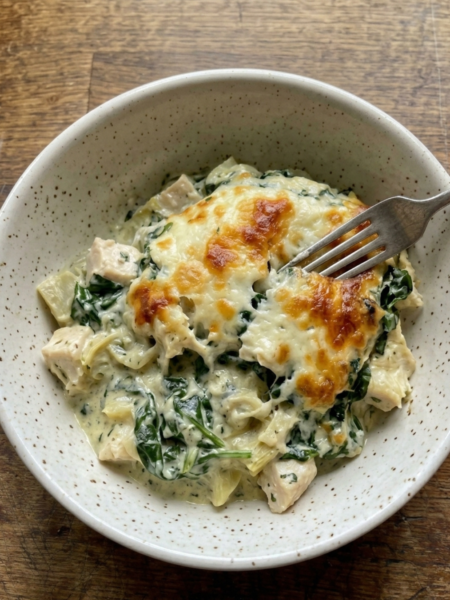Creamy spinach artichoke chicken bake topped with melted mozzarella cheese in a white casserole dish