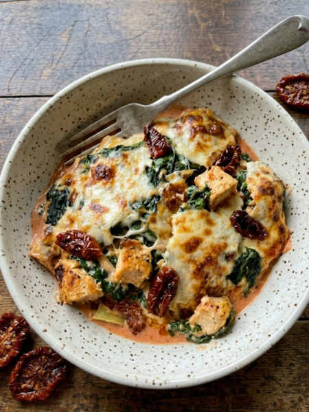 Creamy Tuscan chicken bake with spinach, sun-dried tomatoes, and melted mozzarella cheese in a skillet